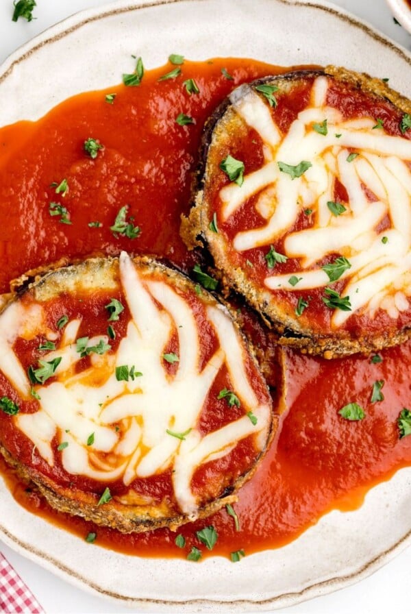 Crispy coated eggplant slices on a white plate covered in marinara sauce and melted cheese