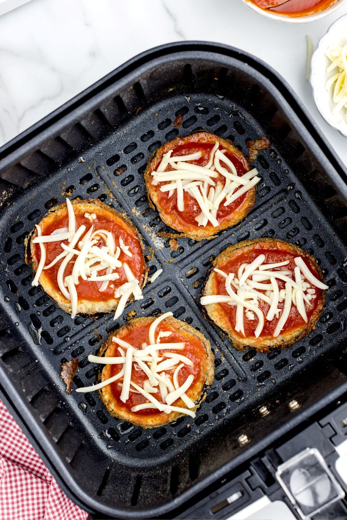 Crispy eggplant sliced with marinara sauce and cheese topped in the air fryer basket.