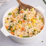 Close-up picture of air fryer fried rice in a large serving bowl with a wooden spoonful of the fried rice.