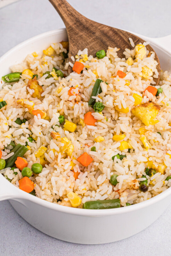 Close-up picture of air fryer fried rice in a large serving bowl with a wooden spoonful of the fried rice.