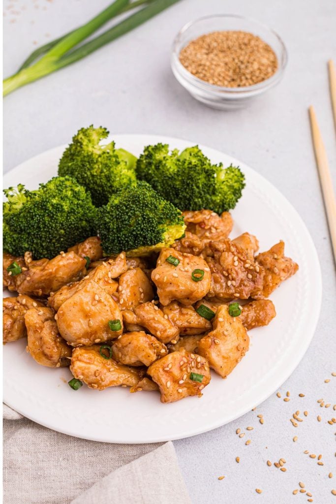 juicy chicken bites in sauce with sesame seeds and broccoli on a white plate. 