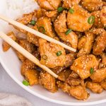 Golden juicy chicken pieces on a white plate being held by chopsticks