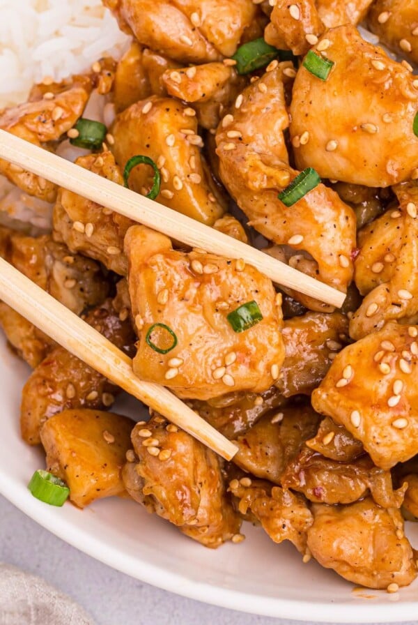 Golden juicy chicken pieces on a white plate being held by chopsticks