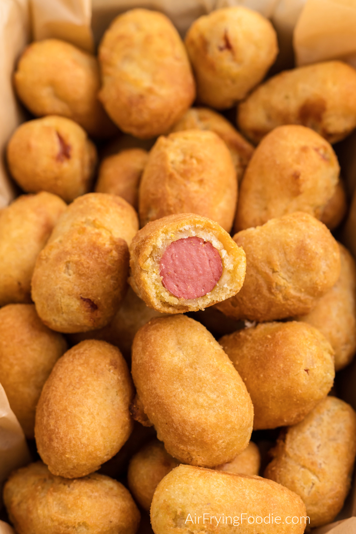 Basket of mini corn dogs made in the air fryer, with one corn dog cut into half.