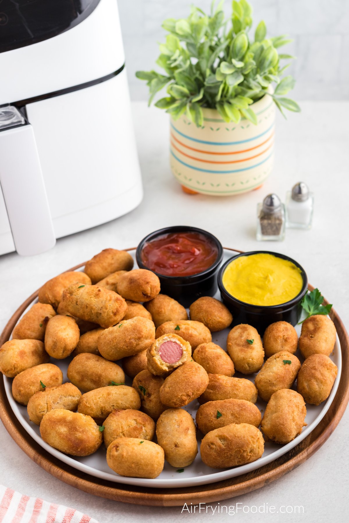 Mini corn dogs in a round plate, made in the air fryer, served with a side of ketchup and mustard.