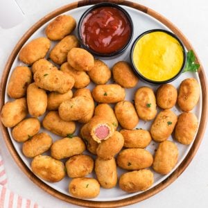 Overhead photo of air fried mini corn dogs on a round plate with a side of ketchup and mustard, ready to eat.