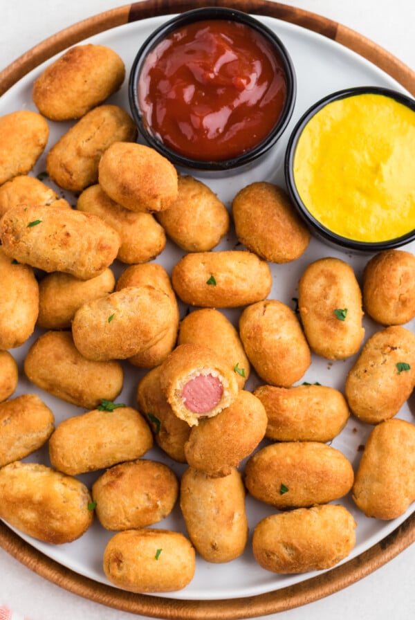 Overhead photo of air fried mini corn dogs on a round plate with a side of ketchup and mustard, ready to eat.