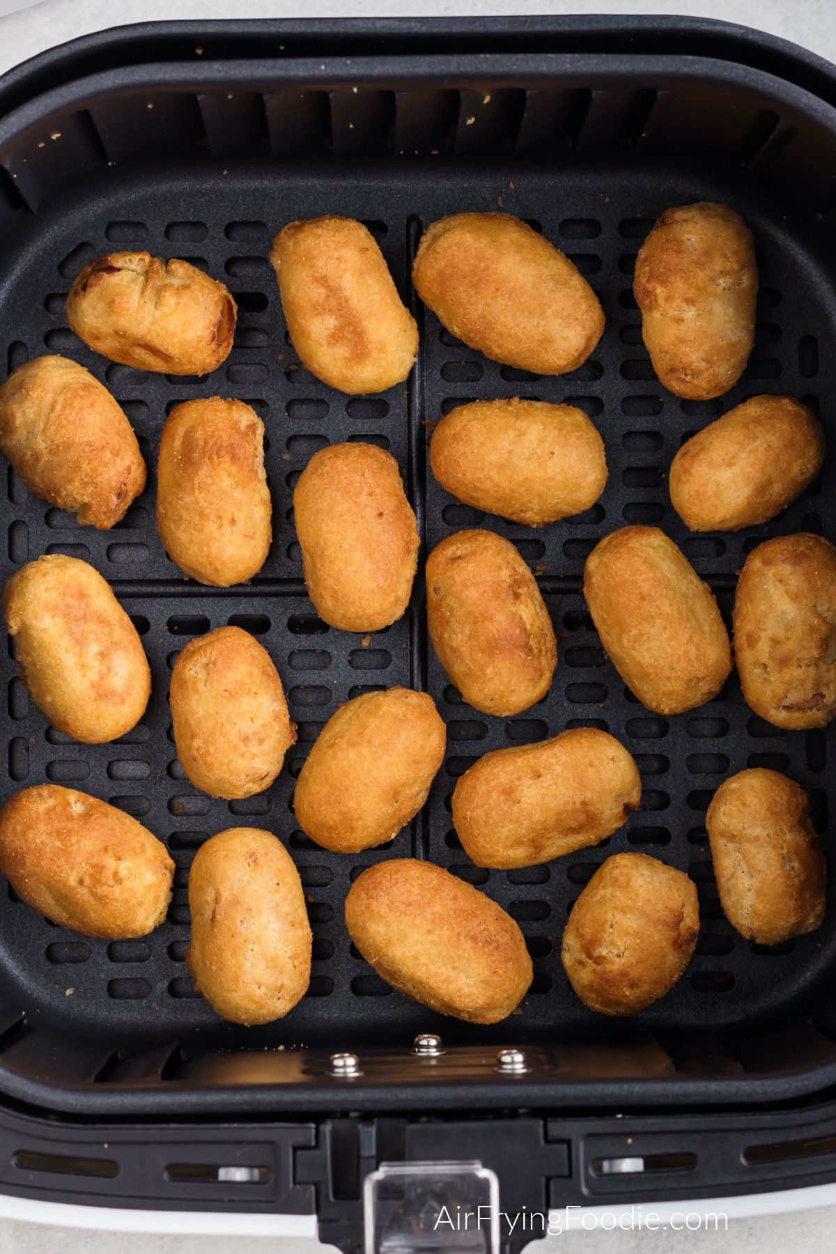 Frozen mini corn dogs in the basket of the air fryer, fully cooked.