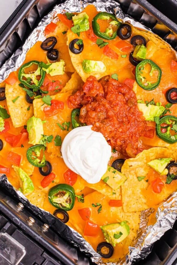 Crispy nachos in an air fryer basket topped with cheese, sour cream and salsa.