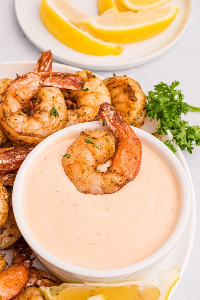 juicy cooked shrimp on a white plate with lemon wedges and a dipping sauce. 