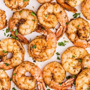 Juicy seasoned shrimp on a white plate garnished with parsley flakes