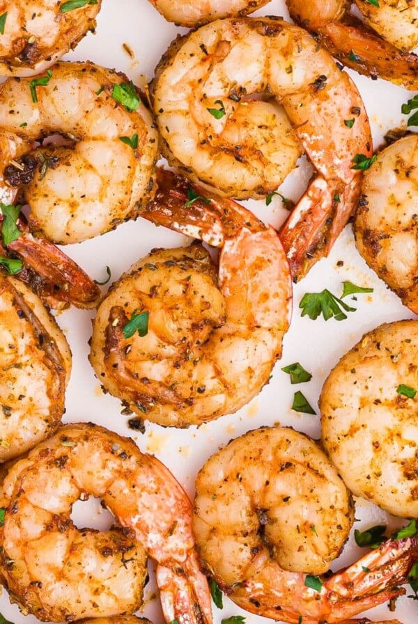 Juicy seasoned shrimp on a white plate garnished with parsley flakes