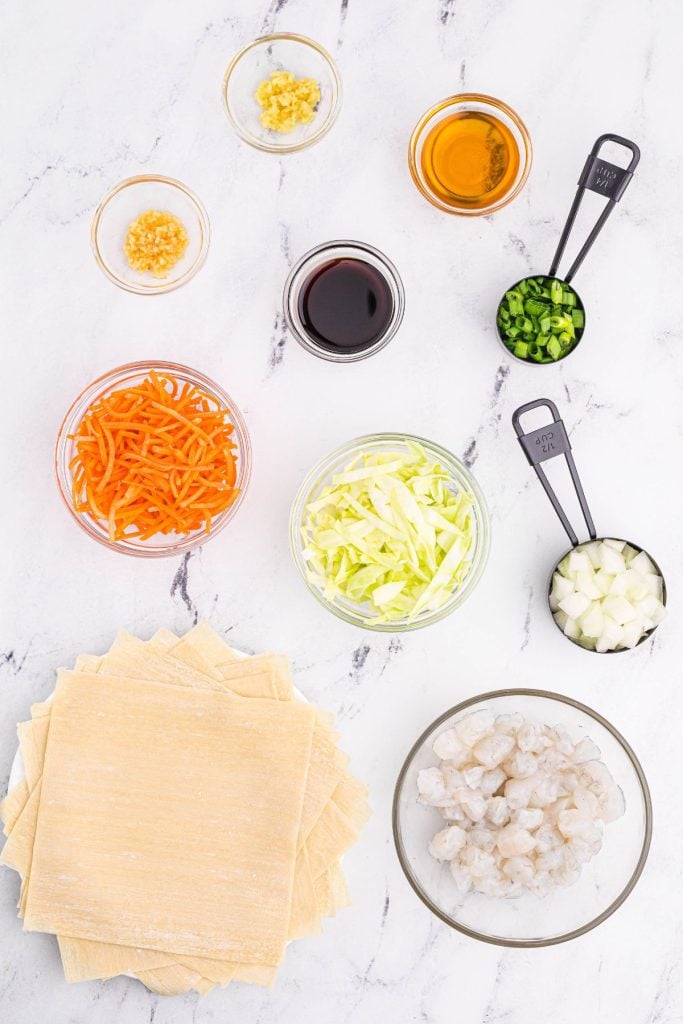 Ingredients needed to make shrimp egg rolls measured out in mixing bowls  on a white marble table 