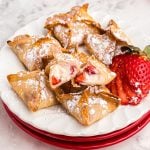 Golden crispy strawberry cheesecake wontons on a white plate with a strawberry