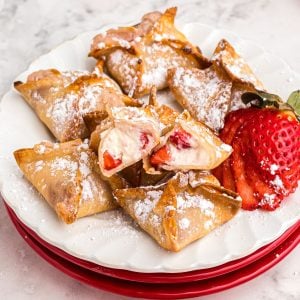 Golden crispy strawberry cheesecake wontons on a white plate with a strawberry