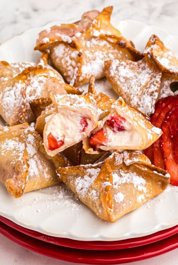 Golden crispy strawberry cheesecake wontons on a white plate with a strawberry