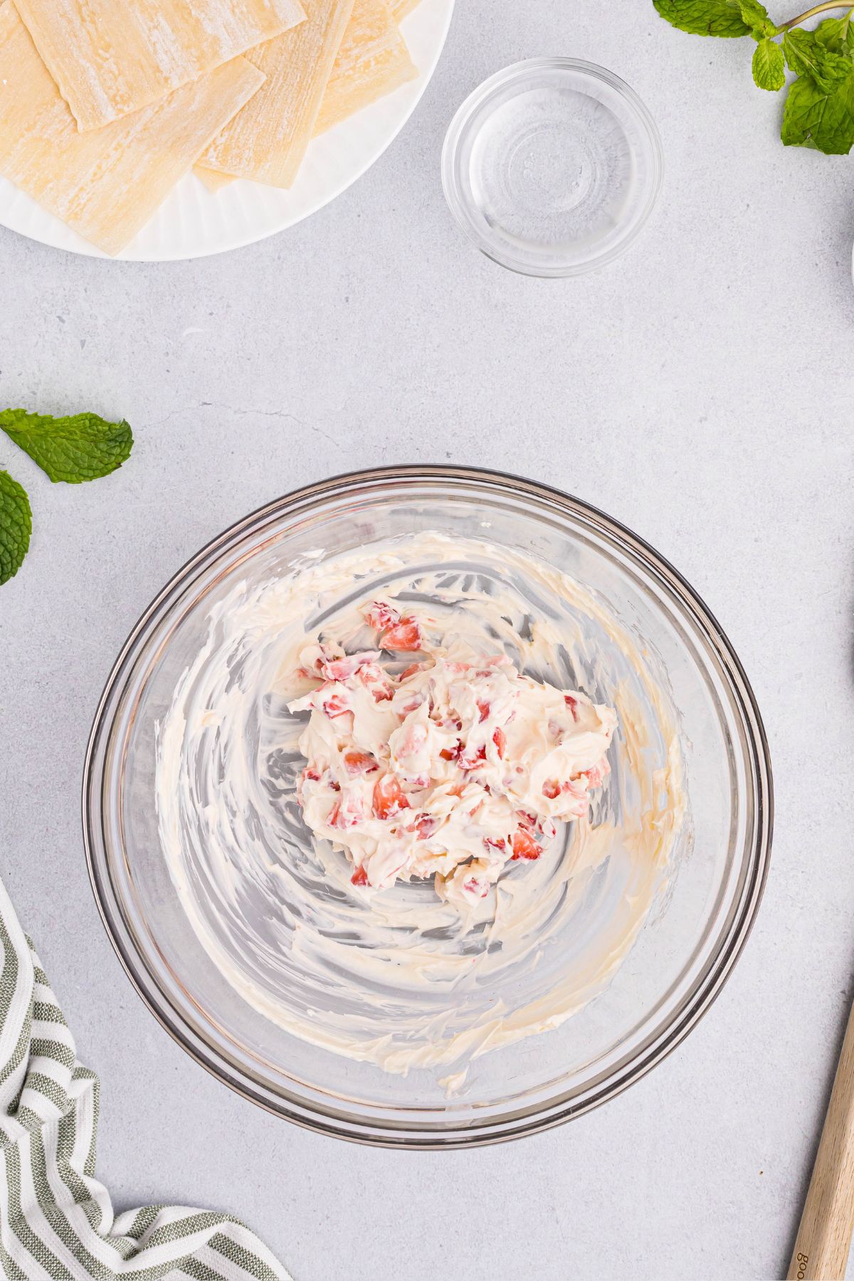 Cream cheese, sugars, and strawberries mixed in a clear glass bowl on a white marble table.