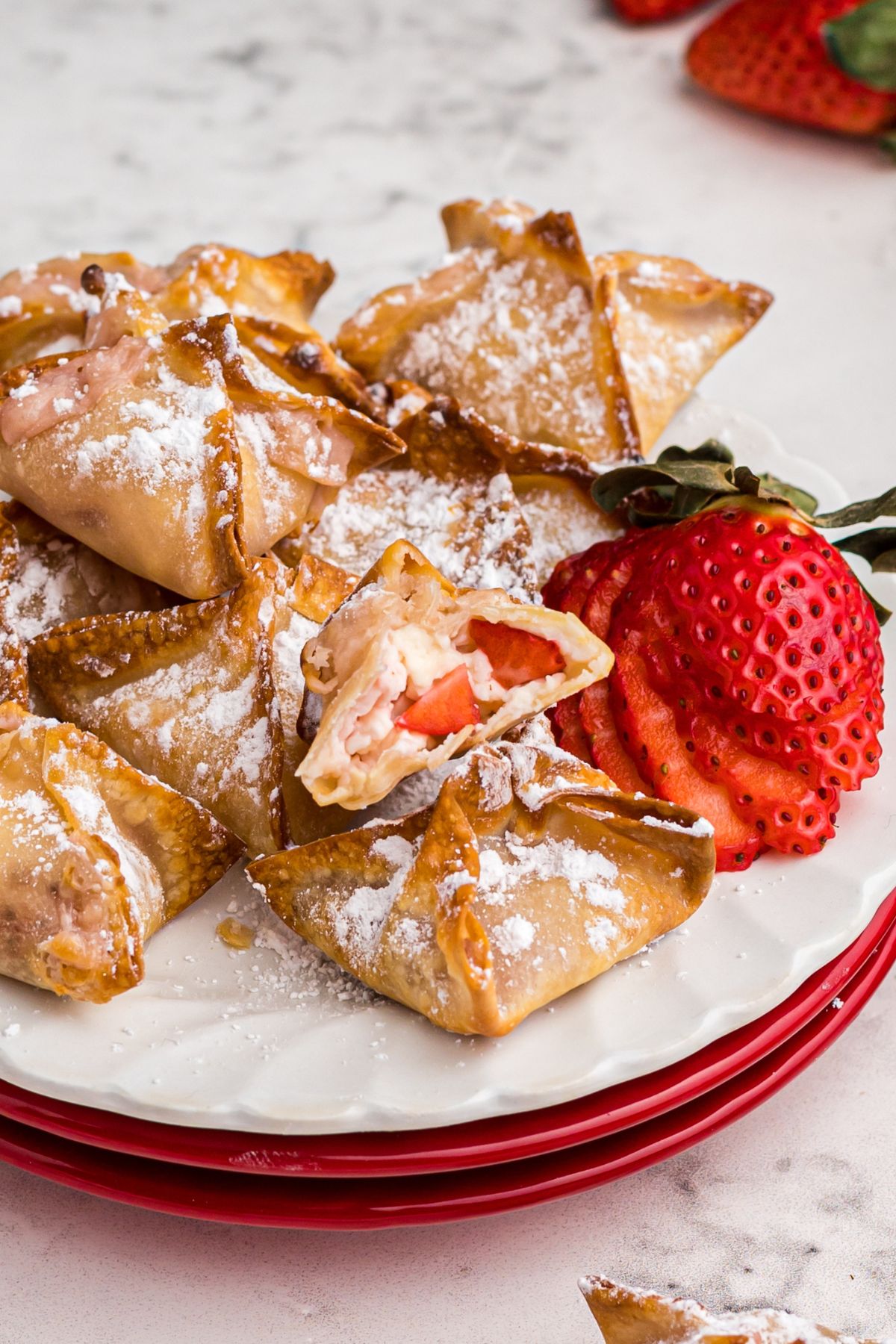 Easy Air Fryer Strawberry Cheesecake Bites 2 Golden crispy wontons filled with creamy cheesecake and fresh strawberries, lightly dusted with powdered sugar.