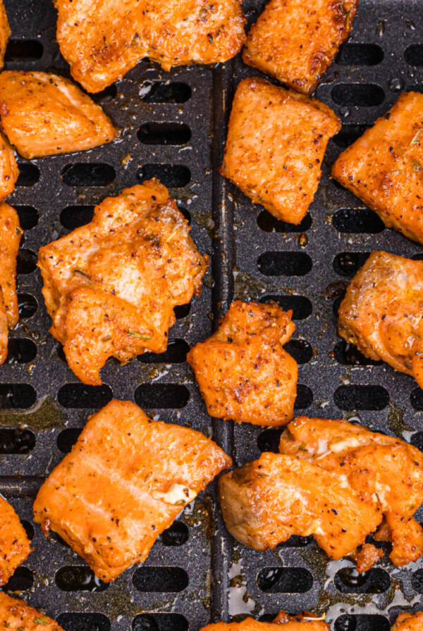 Blackened salmon bites in the basket of an air fryer.