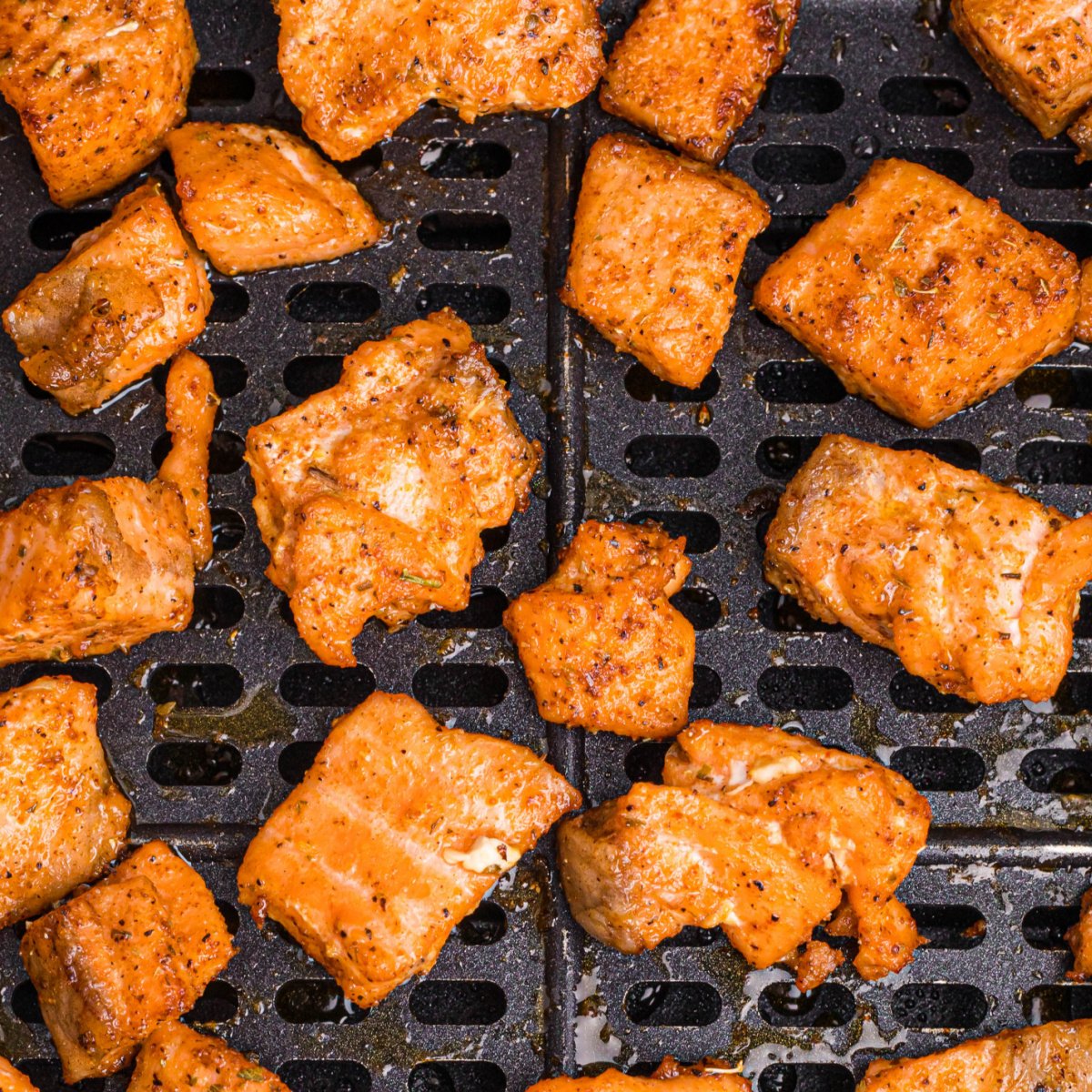 Blackened salmon bites in the basket of an air fryer.