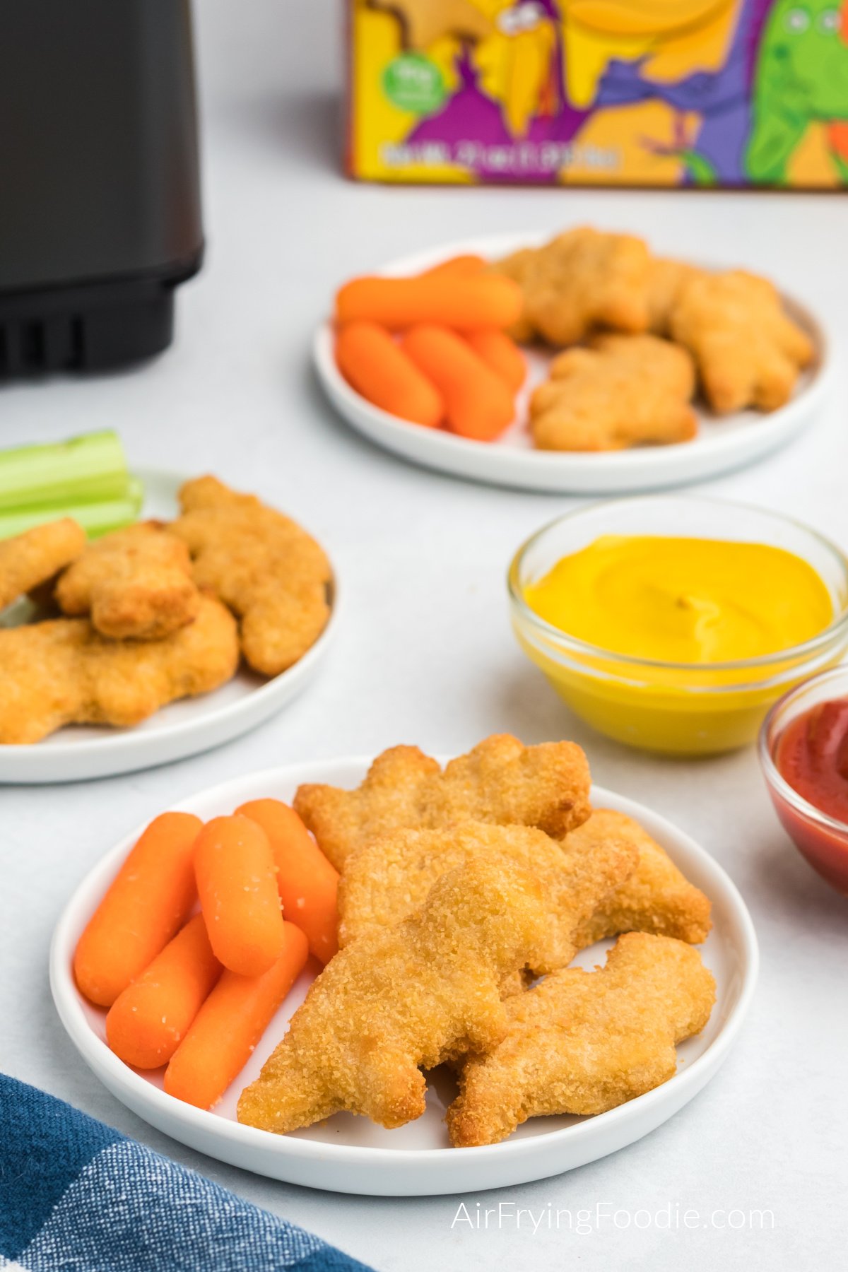 Dino nuggets made in the air fryer, served on plates with carrots and sides of ketchup and mustard.