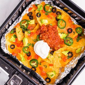 Nachos with melted cheese and toppings in the air fryer basket.
