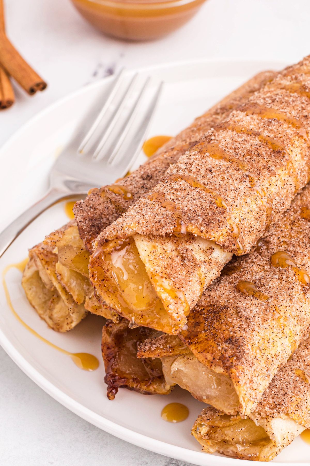 Apple pie taquitos made in the air fryer, on a white plate with a fork.