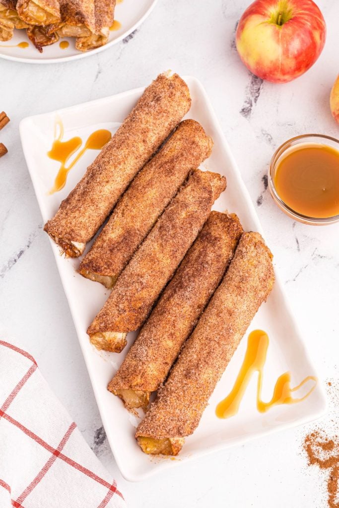 Golden sugar and cinnamon coated taquitos on a white plate with caramel drizzle sauce