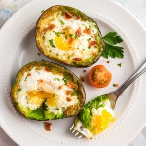 Juicy avocados sliced open with egg cooked in center on a white plate.