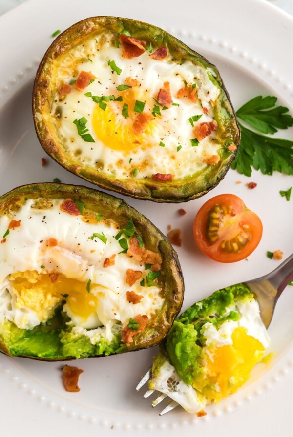 Juicy avocados sliced open with egg cooked in center on a white plate.