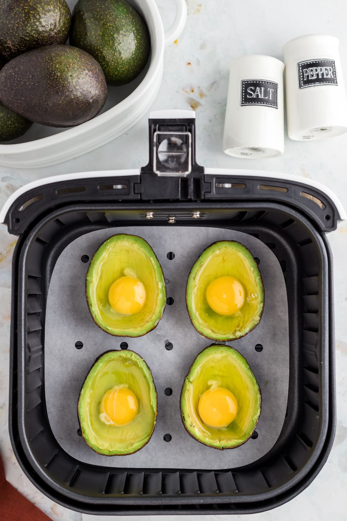 Avocados sliced in half and then filled with raw eggs in the air fryer basket.