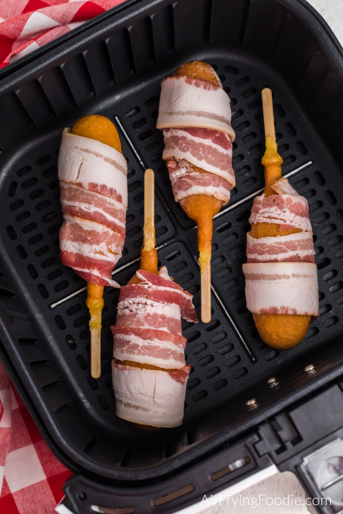 frozen corn dogs wrapped in bacon and placed in a single layer in the basket of the air fryer.