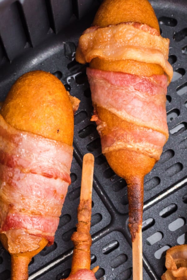 Bacon wrapped corn dogs in the air fryer basket, ready to serve.