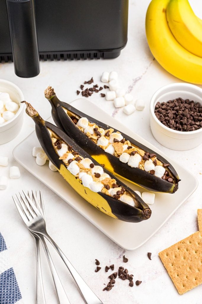 Bananas split open and filled with marshmallows and chocolate chips on a white plate.