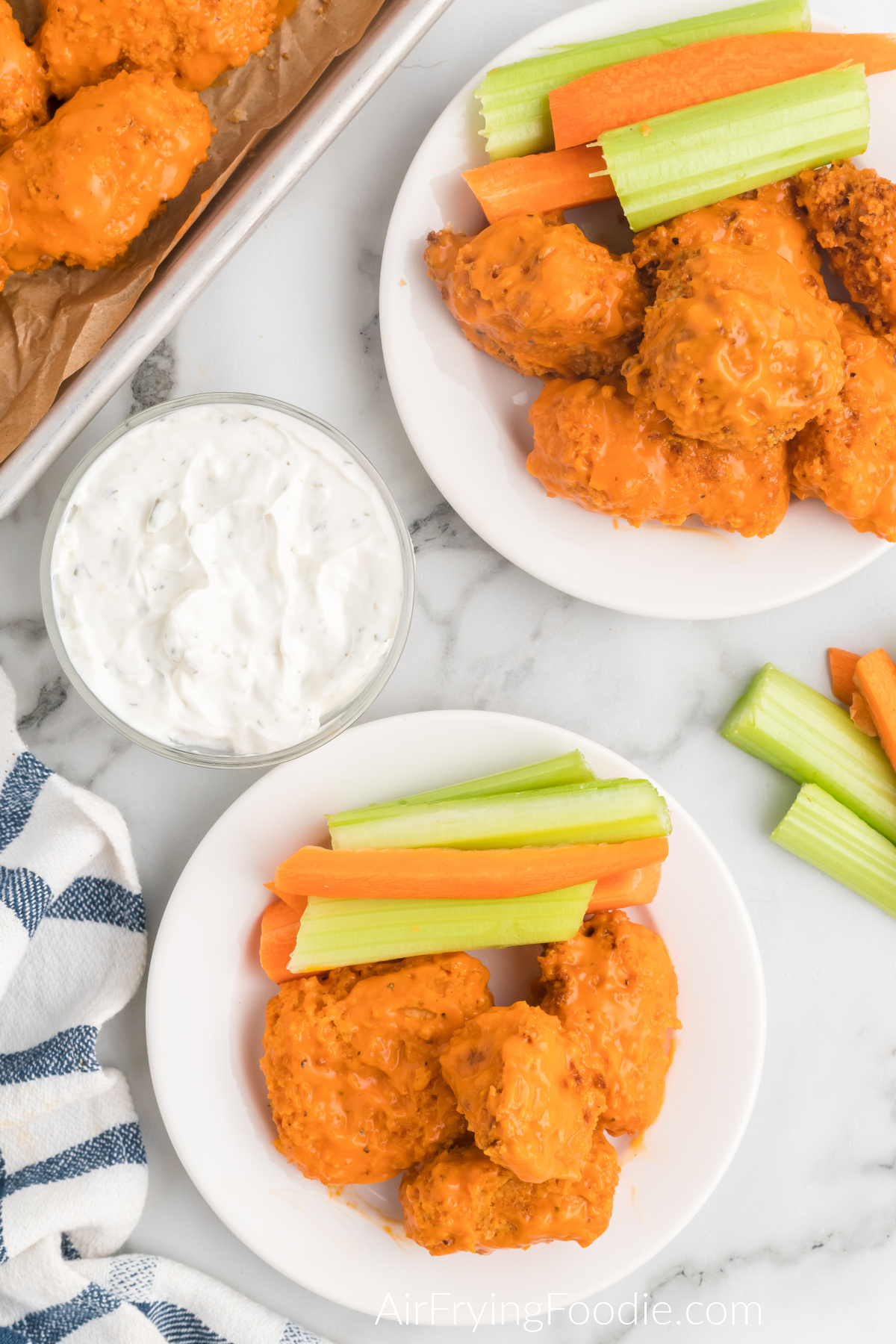 Wings topped with sauce and served on a plate with celery and carrots. 