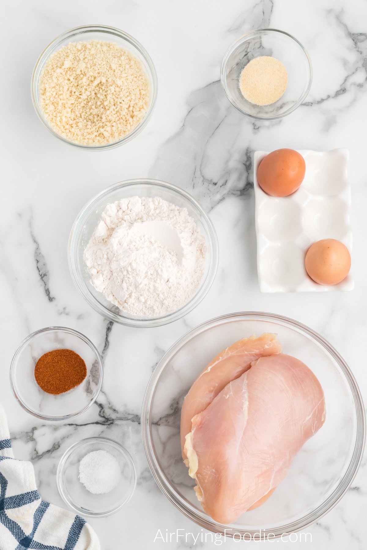 chicken breast, flour, seasoning, eggs, and breadcrumbs on a white table to make boneless chicken wings. 