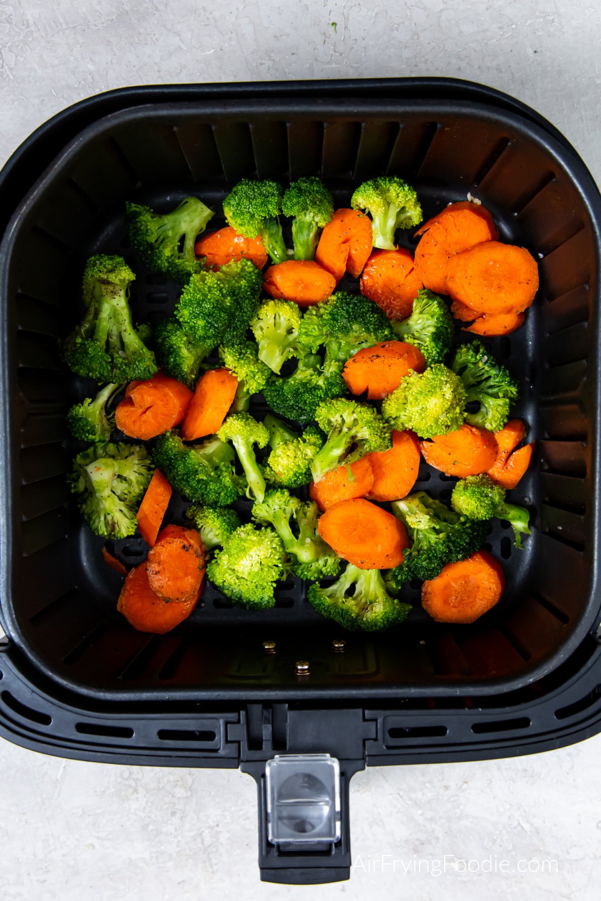 Freshly seasoned broccoli and carrots in the basket of the air fryer.Ready to cook.