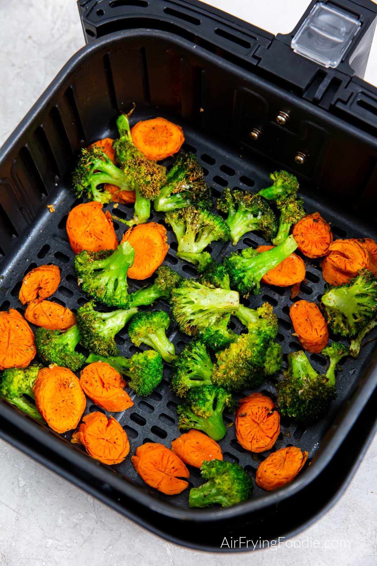 Seasoned and air fried carrots and broccoli in the basket of the air fryer.