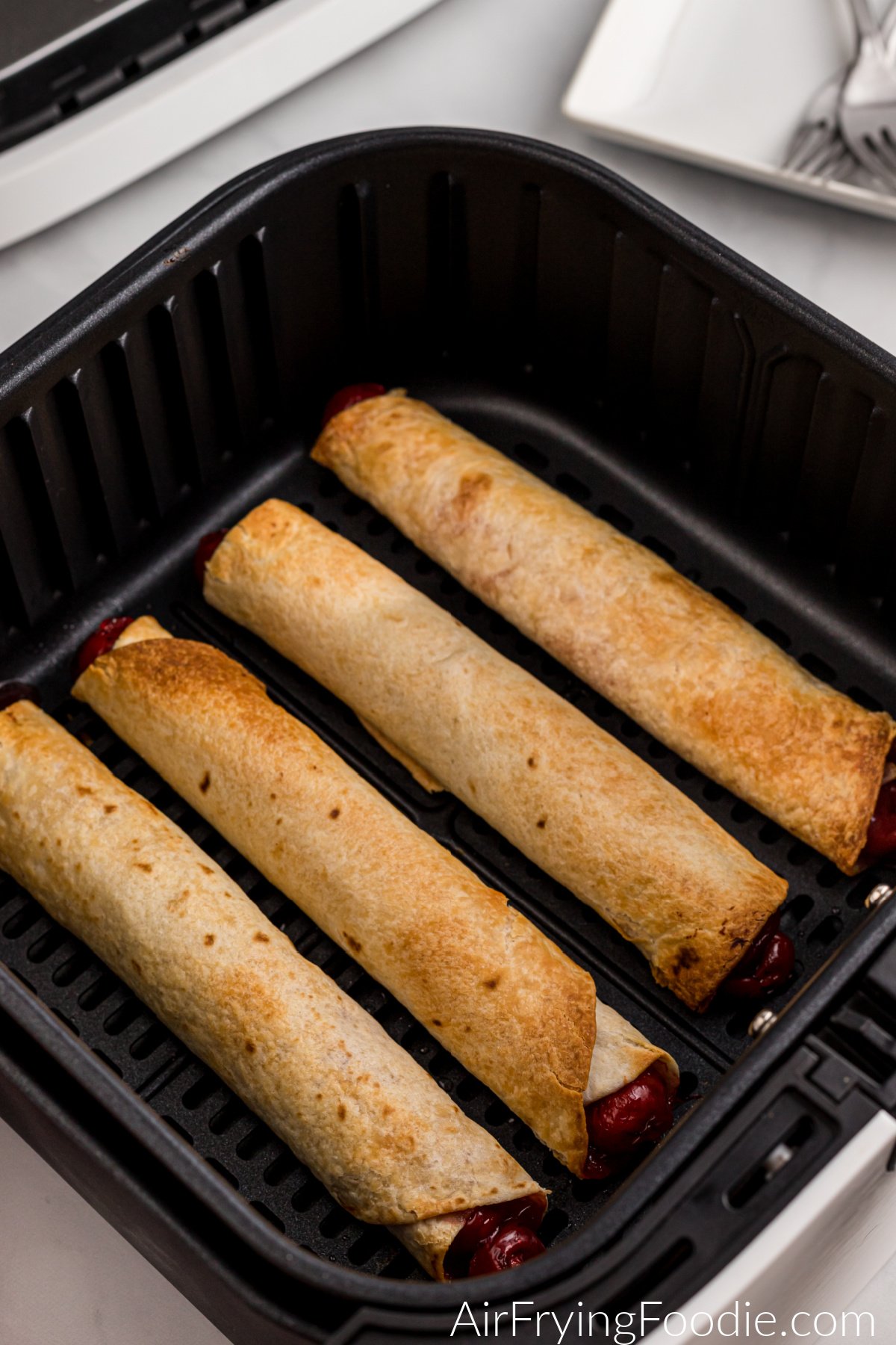 Golden brown air fryer cherry pie taquitos in the basket of the air fryer.