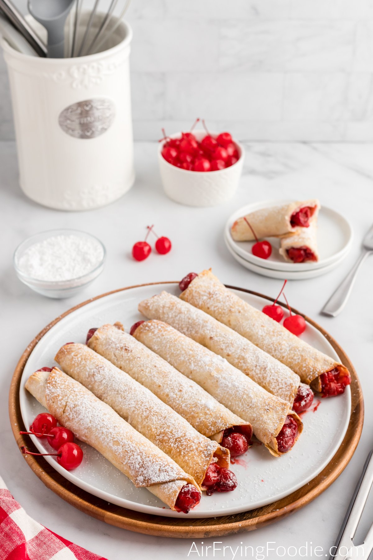 Cherry pie taquitos made in the air fryer and served on a plate dusted with sugar.
