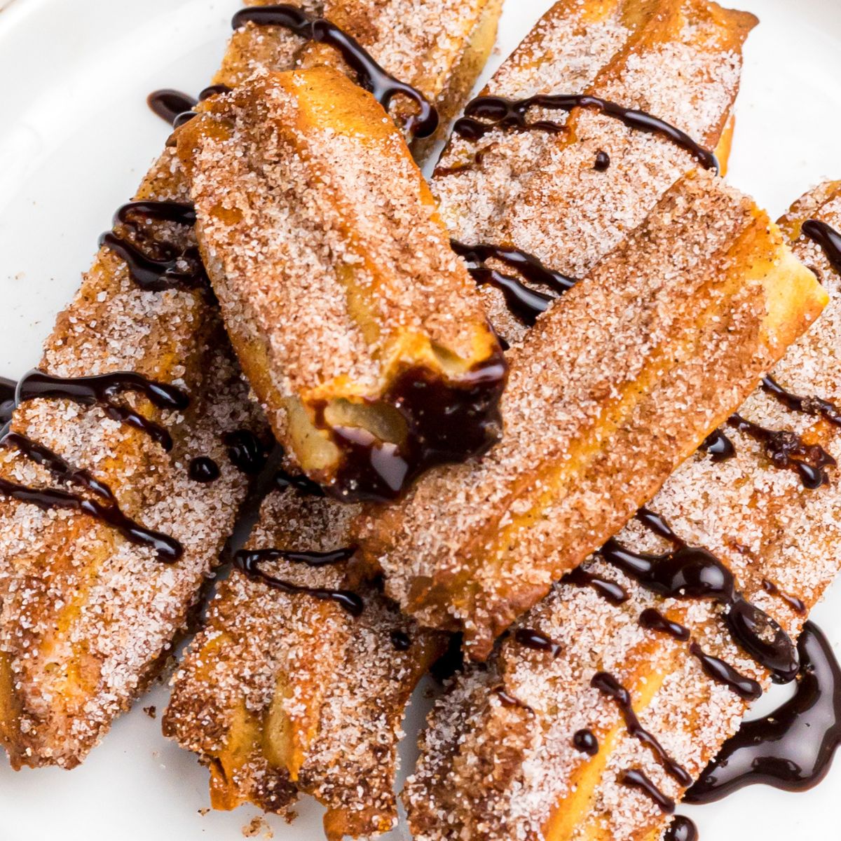 Golden sugar and cinnamon coated churros on a white plate drizzled with chocolate