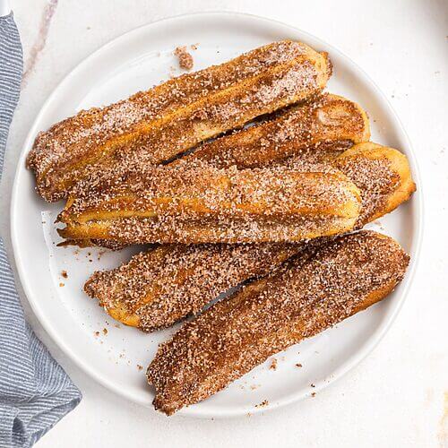 Cinnamon and sugar coated churros on a white plate
