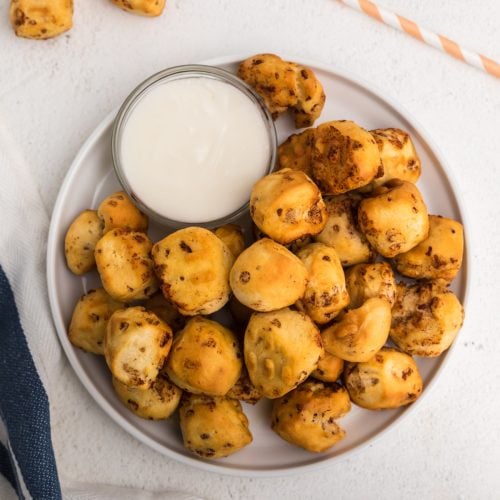 Overhead photo of air fryer cinnamon roll bites in a white plate with icing for dipping.