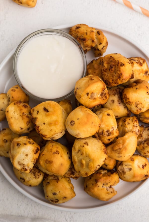 Overhead photo of air fryer cinnamon roll bites in a white plate with icing for dipping.