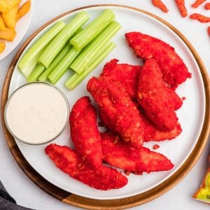 Red Cheeto coated chicken tenders on a white plate with celery and ranch