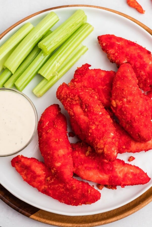 Red Cheeto coated chicken tenders on a white plate with celery and ranch