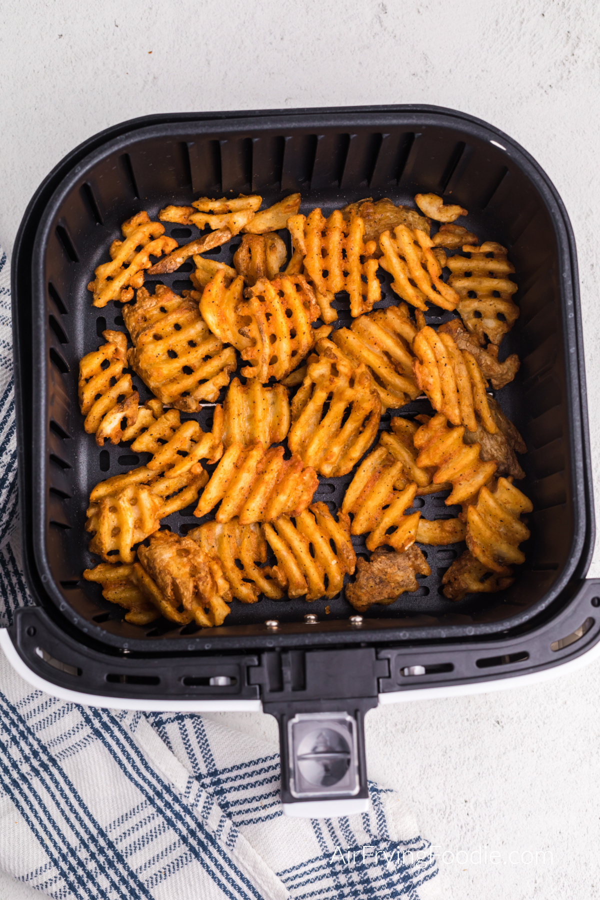Air fried frozen waffle fries in the basket of the air fryer, ready to serve.