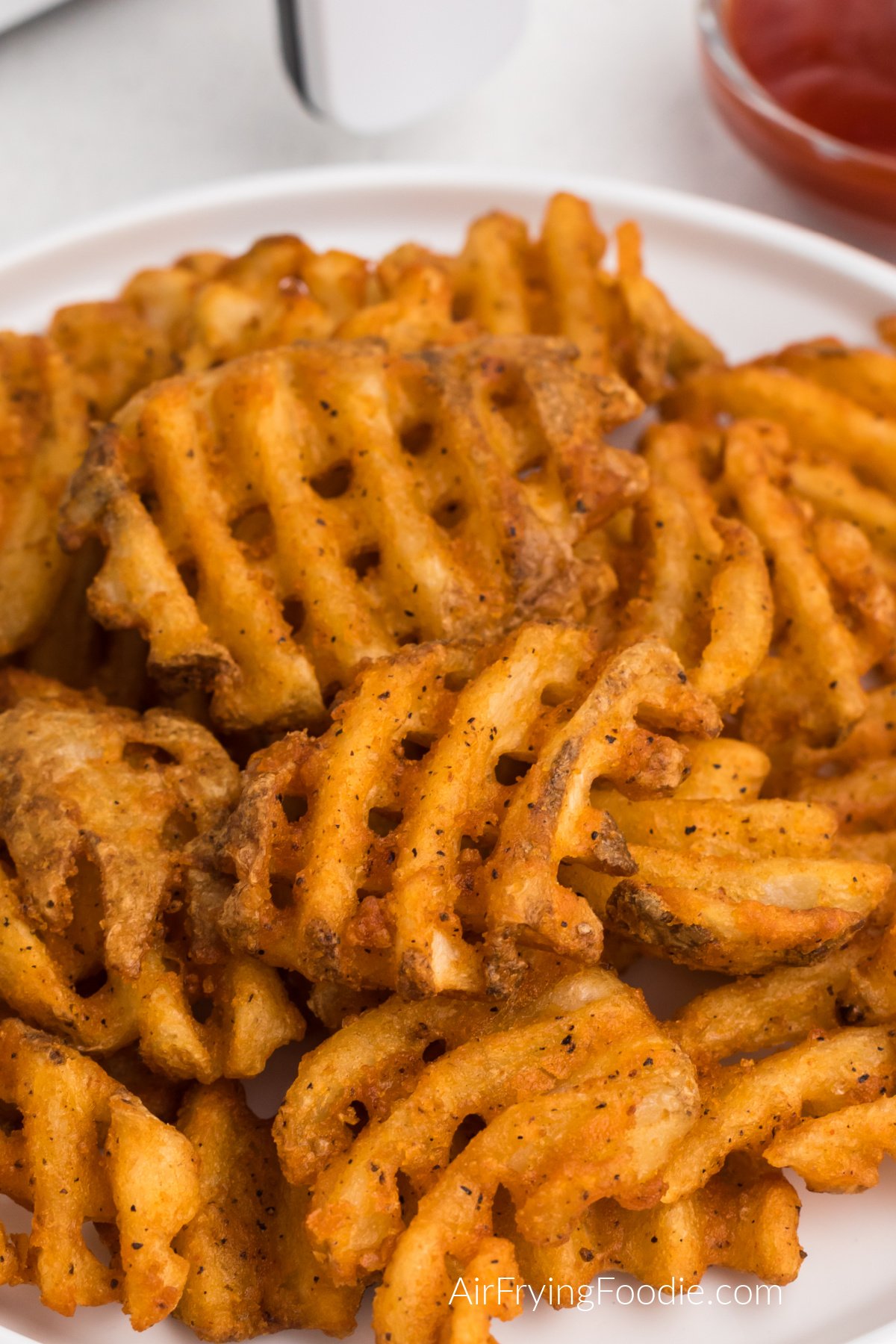 Seasoned waffle fries made in the air fryer and served on a white plate. 