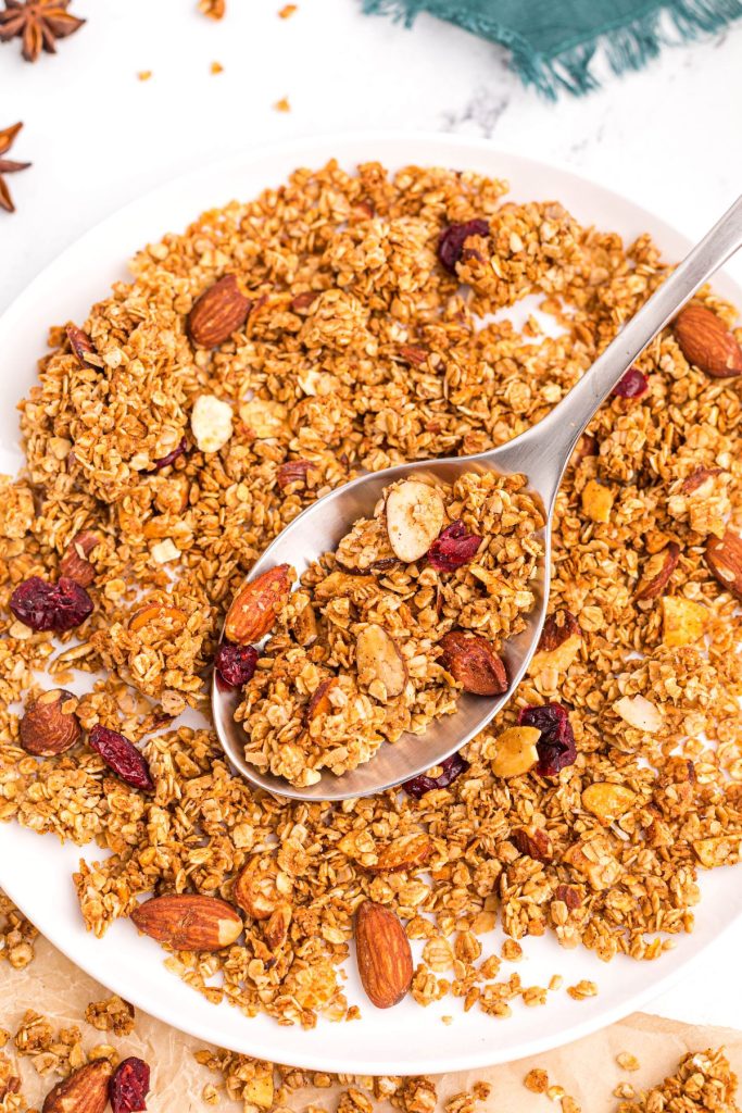Spoonful of golden crispy granola mixed with nuts and dried fruit in a white bowl. 