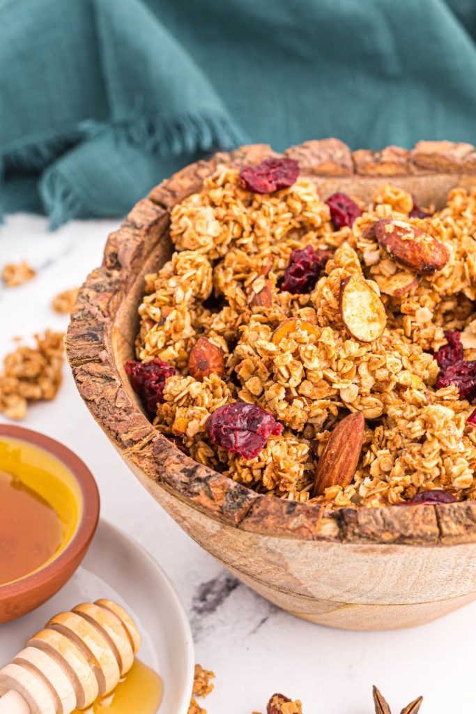 Golden brown oats mixed with nuts and dried fruit in a wooden bowl on a marble table. 
